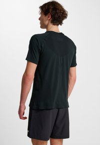 Zwarte sportieve kortemouwen shirt met een gladde textuur, voorzien van raglanmouwen en een ronde zoom, gedragen met donkere shorts.