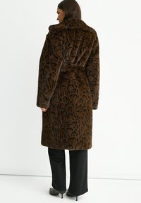 Brown leopard print faux fur coat with a high collar, belted waist, and long sleeves, paired with black pants and heeled shoes.