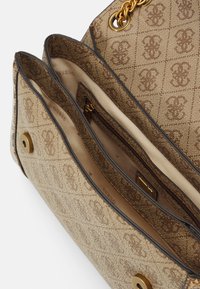 Brun mønstret stof håndtaske med to hovedrum, en lynlåslomme indeni og detaljer med kædetræk i guldfarve.