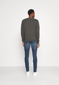 Graues Langarmshirt, schlanke blaue Jeans und weiße Sneakers. Das Shirt hat einen runden Ausschnitt und gerippte Bündchen.