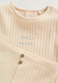 Body beige côtelé pour bébé avec texte "hello world." en gris et pantalon côtelé assorti avec deux boutons à la ceinture avant.