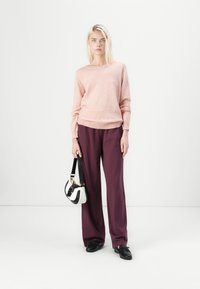 Light pink sweater with ribbed hem, paired with loose-fitting burgundy trousers. Accessory is a small, black and white handbag. Black shoes.