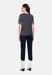 Gray short-sleeve top with floral embroidery on sleeves, paired with dark blue jeans and white heeled boots. Smooth texture, relaxed fit.