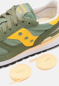 Green suede and mesh sneaker with yellow accents and a white midsole. Includes two coiled yellow laces beside the shoe.
