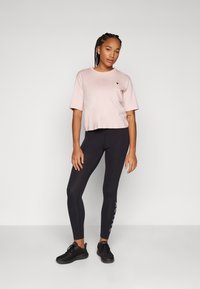 T-shirt cropped rosa claro com mangas curtas e um pequeno logotipo preto, combinado com leggings pretas que possuem um detalhe colorido com palavras de um lado.