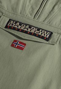Lekka, khaki zielona kurtka z czarną i beżową naszywką z logo oraz małą wyszywaną flagą norweską z przodu.
