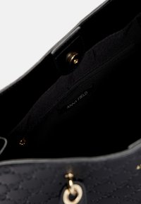 Interno di una borsa nera con una tasca con zip, chiusura magnetica dorata e etichetta del marchio Anna Field visibile all'interno.