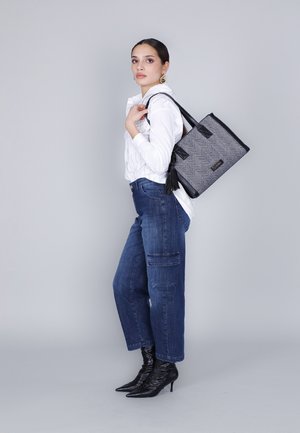 Zwart en grijs visgraat handtas met kwast, twee korte handvaten en gestructureerd ontwerp, gecombineerd met losse denim en zwarte puntige laarzen.