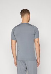 Camiseta deportiva gris de manga corta con cuello redondo y costuras visibles. Presenta la marca "NIKE PRO" en la parte posterior del cuello. Textura suave.