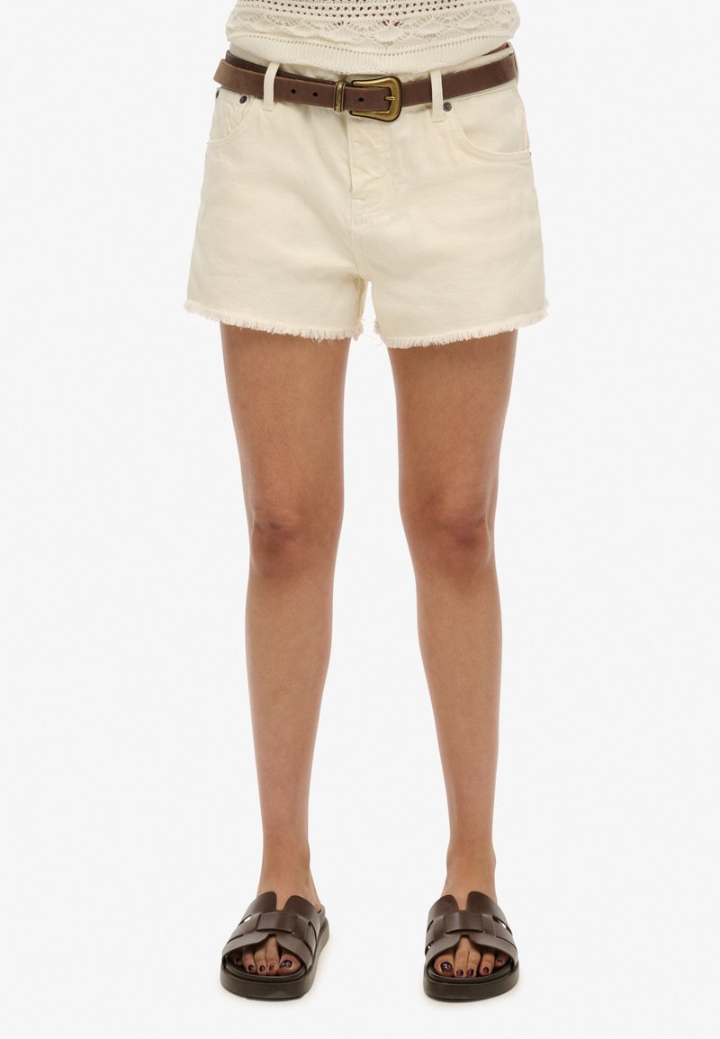 Shorts de mezclilla color crema con los bordes deshilachados, con un cinturón de cuero marrón y hebilla dorada. Combinados con sandalias de tiras marrones oscuras.