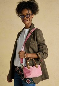 Ružová kabelka s hnedými koženými detailmi, hladká textúra, malá veľkosť, v kombinácii s károvaným sako a neformálnym bielym tričkom.