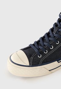 Marineblå canvas høyhælte sneakers med gummitåhette, hvit såle og marineblå snøringer. Har sømdetaljer og små merkevareelementer.