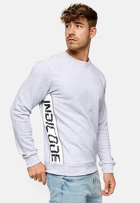 Sweatshirt gris avec des manches longues, un col rond et un logo noir audacieux courant verticalement sur un côté. Texture lisse.