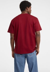 Bordo medvilnės T-shirt su trumpomis rankovėmis, apvalia iškirpte ir laisvu pajamumu. Ypatumai: lygus paviršius, matoma siūlė ir be grafikos.