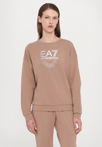 Barna pamut pulóver kerek nyakkivágással, hosszú ujjakkal, és ezüst színű logónyomattal az elején. Puha tapintás, laza szabás.