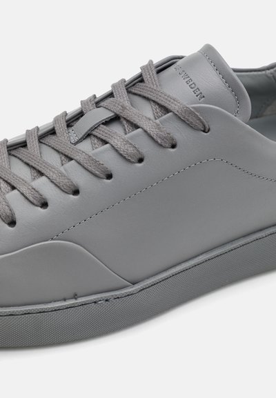 Szürke sneaker sima bőrből, szürke fűzőkkel, gumitalppal és minimalista dizájnnal, finom varrási részletekkel.
