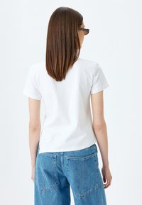 Camiseta de algodón blanca con mangas cortas, corte relajado y cuello redondo, combinada con pantalones de mezclilla azul de cintura alta con bolsillos traseros.