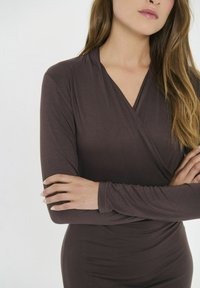 Dolga rokav zavita majica v temno rjavi tkanini, ki ima obliko V-izreza in mehko teksturo, z navzkrižno sprednjo stranjo in oprijetim silhuetom.
