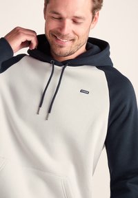 Hooded sweatshirt with a light gray body and dark blue raglan sleeves. Features a front pocket and drawstrings with metallic tips.