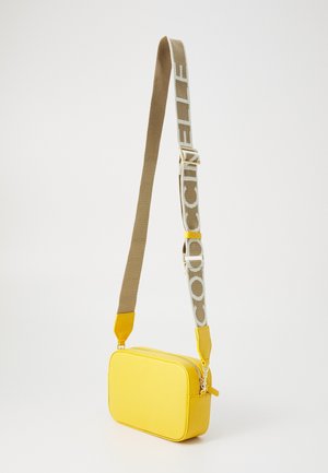Sac bandoulière rectangulaire jaune avec surface texturée et sangle beige réglable avec un grand texte blanc.