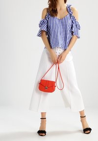Blå och vit rutigt topp med avskuren sommar-ruffle, matchat med vita vida byxor. Röd axelväska, svarta klacksandaler med fransar.