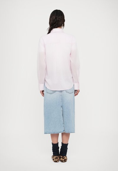 Ροζ ανοιχτό πουκάμισο με μακριά μανίκια, συνδυασμένο με μπλε τζιν μίντι φούστα και παπούτσια με λεοπάρ μοτίβο, φωτογραφημένα από πίσω.