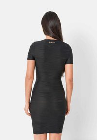 Robe noire moulante à manches courtes, en tissu texturé présentant des motifs en vagues, avec un accent de logo doré au niveau de l'encolure au dos.