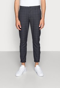 Chinos van donkere geruite stof, met een aansluitend ontwerp, enkellang, minimale ritsaccenten bij de manchetten, gecombineerd met witte sneakers.
