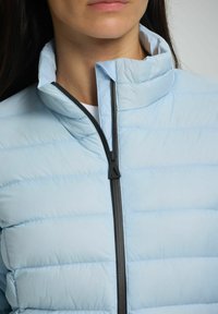 Giacca puffer azzurro chiaro con colletto alto, caratterizzata da cuciture orizzontali, zip nera e una superficie liscia.