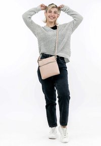 Borsa a tracolla rosa chiaro con tasca frontale con zip, finitura testurizzata e tracolla regolabile, abbinata a un maglione grigio a maglia e jeans neri.