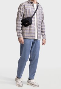Camisa de cuadros de manga larga en beige y azul, camiseta blanca debajo, jeans azul claro, bolso de mano negro y zapatillas metálicas.