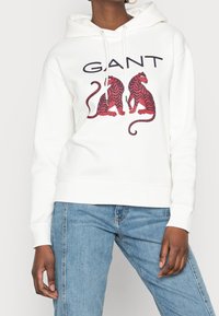 Sudadera blanca con un gráfico frontal de dos tigres a rayas rojas y negras. Cuenta con capucha con cordón y puños y dobladillo acanalados.