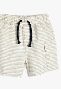 Lysebeige shorts med vandrette striber, elastisk talje og mørkeblå snor. Har en sidelomme til opbevaring. Blød tekstur.