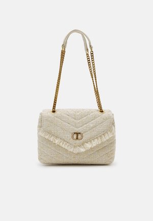 Kremowa torebka na ramię z teksturowanej tkaniny, z złotymi łańcuszkowymi paskami, wykończona frędzlami oraz małą ozdobną metalową klamrą na przednim klapie.