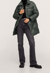 Grøn polstret frakke med høj krave, quiltet design, frontlynlås og to brystlommer. Kombineret med mørkegrå lige ben jeans og sorte støvler.