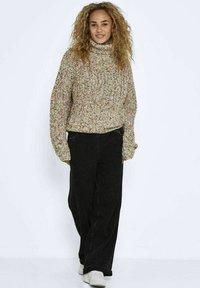 Chunky gebreid turtleneck sweater in morekleurige vezels, gecombineerd met losse zwarte denim broek en witte sneakers, gedragen door een persoon die staat.