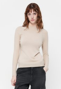 Beige stripete strikkegenser med lange ermer, høy hals og tettsittende fasong; myk tekstur, passer med mørke bukser.