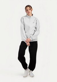 Jasnoszara bluza polarowa z suwakiem do połowy długości i bocznymi kieszeniami, połączona z czarnymi spodniami dresowymi i białymi trampkami, z detalem logo.