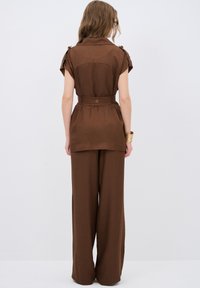 Completo beige composto da top a maniche corte con cintura e pantaloni a gamba larga, realizzati in un tessuto morbido con una vestibilità rilassata.