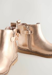 Stivaletti alla caviglia color rosé metallizzato con finitura in pelle liscia, cerniere laterali e linguette decorative; dotati di una suola in gomma durevole.