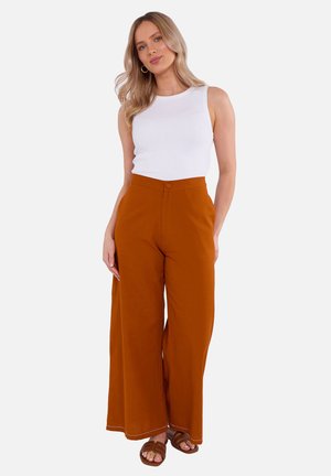 Witte mouwloze top met ronde hals en oranje broek met wijde pijpen, voorzien van een sluiting met knopen aan de voorkant en contrasterende witte stiksel.