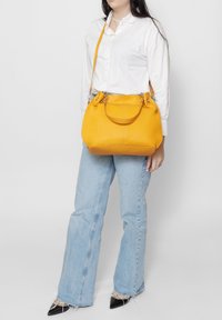Gele leren handtas met een gestructureerde vorm, dubbele bovenhandvatten en een verstelbare schouderriem. Soepele textuur en verfijnde stiksels.