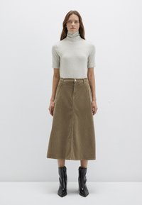 Light gray, short-sleeve turtleneck top paired with a long, khaki corduroy skirt and black, ankle-height, pointed-toe boots.