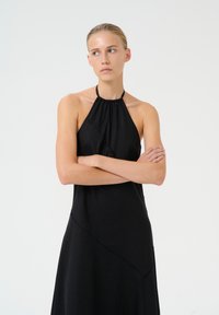 Črna obleka s halter izrezom iz teksturirane tkanine, ki ima oprijet bodice in A-linijski kroj, okrašena z diagonalnimi šivi.