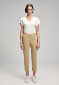 Top bianco a V con maniche corte, abbinato a pantaloni beige chiaro su misura e sneakers bianche. Design semplice con una silhouette aderente.