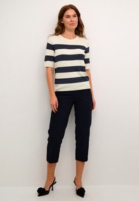 Strikket stripete topp i krem og marineblå, med korte ermer og rund hals, kombinert med marineblå cropped bukser og svarte hælede sko.
