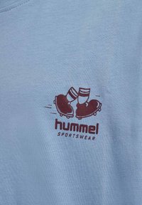 Logo med to fødder iført fodboldstøvler, der klirrer sammen over teksten "hummel SPORTSWEAR" på lyseblåt stof.