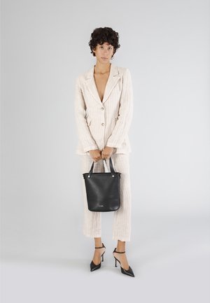 Lys linned blazer og bukser sæt med lodrette striber, parret med en sort læder tote taske og spidse stiletter. Neutral baggrund.