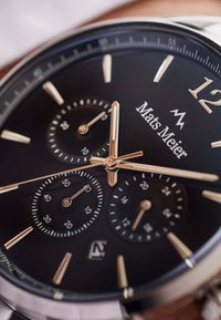 Black watch face with silver and gold accents. Features three sub-dials, date display, and bold hour markers. Smooth metal case and lugs.