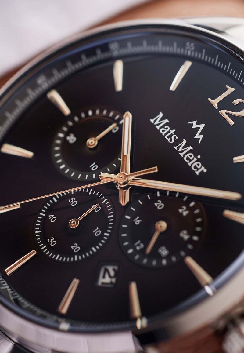 Black watch face with silver and gold accents. Features three sub-dials, date display, and bold hour markers. Smooth metal case and lugs.